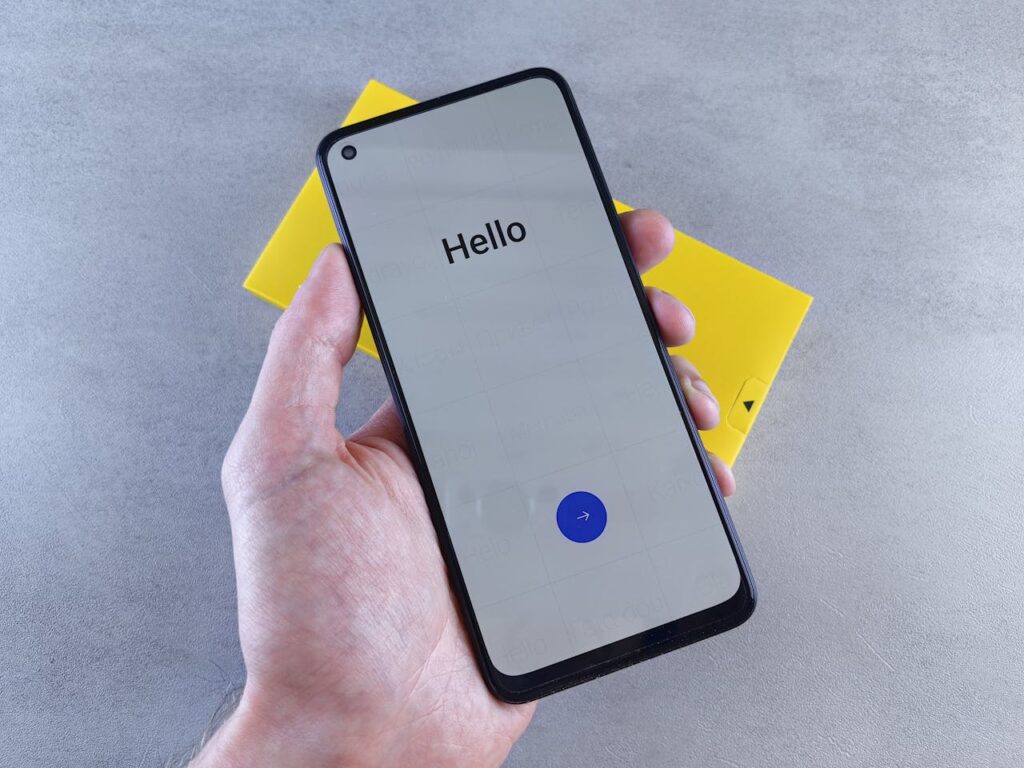 pexels-photo-26443416 A hand holding a smartphone displaying 'Hello' on a gray surface with a yellow box underneath.