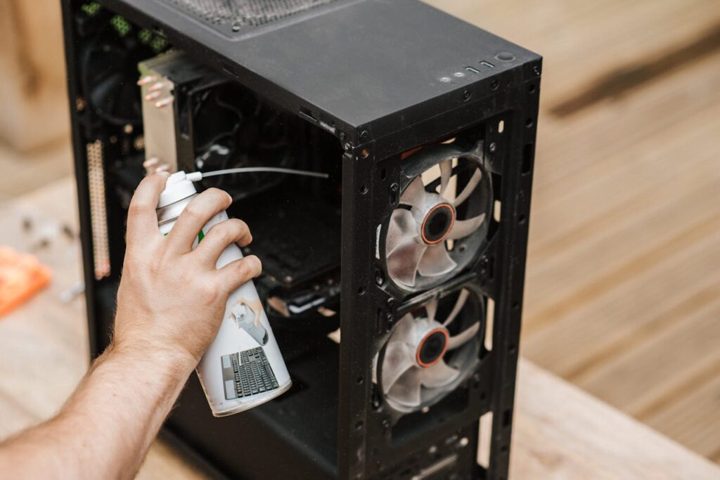 pexels-photo-4792719 A person using compressed air to clean a computer case, focusing on dust removal.